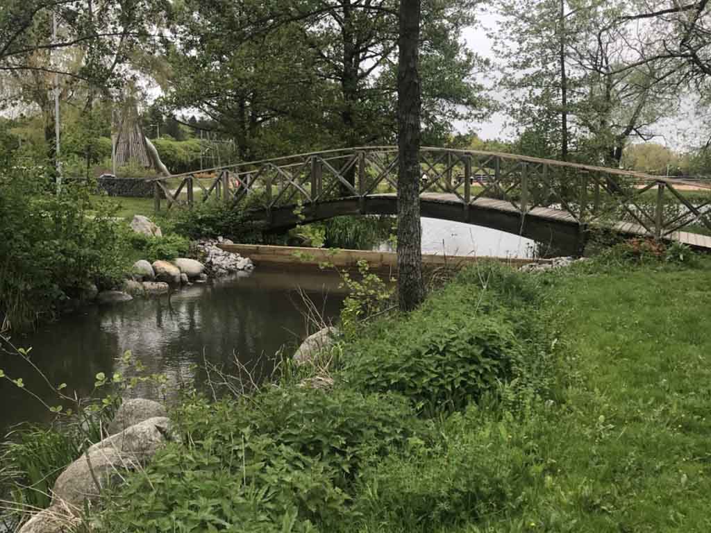 Bro över vattenfyllt dike vid Lögarängen med träskärm under
